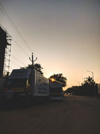 Cars on street by buildings against sky during sunset