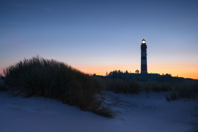 Lighthouse amidst buildings against sky during winter