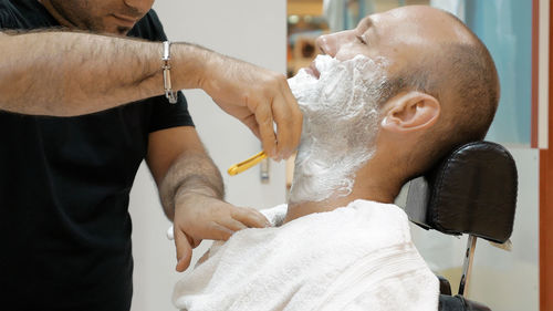 Midsection of barber doing shaving of mature man in salon