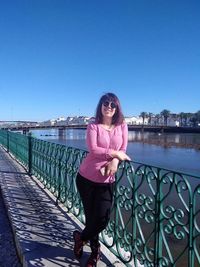 Woman standing by railing against clear blue sky