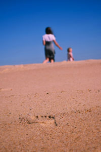 Rear view of woman with daughter walking on sand at beach