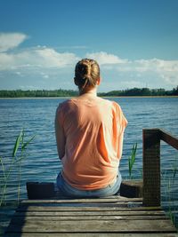 Rear view of woman sitting on pier by lake