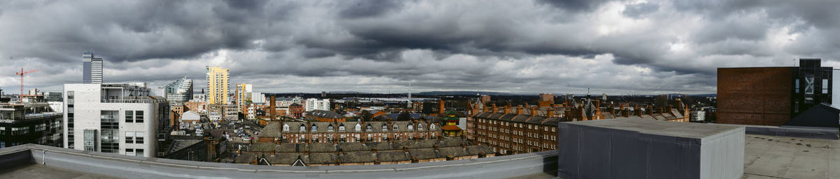 Panoramic view of city buildings against cloudy sky