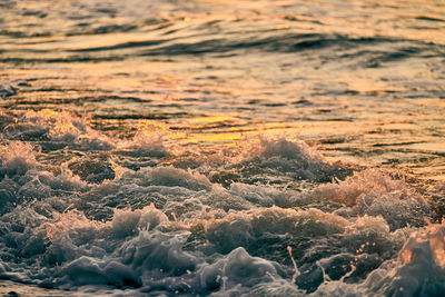 Atmospheric sea foam at colorful sunset, beautiful scene of deep sea waves in gold water sparkles