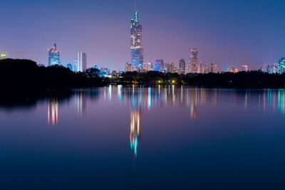 Illuminated buildings by lake against sky at night