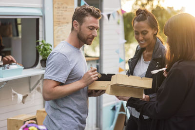 Smiling friends holding disposable food boxes outside food truck