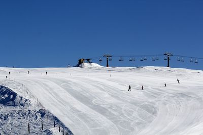 People skiing on snow covered landscape against clear blue sky