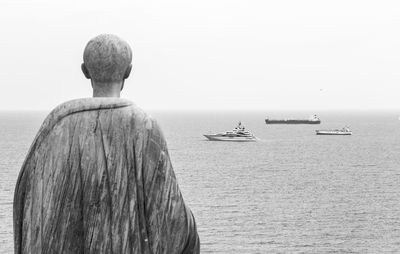 Rear view of sculpture looking at sea against clear sky