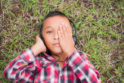 High angle portrait of boy listening music while lying on grassy land