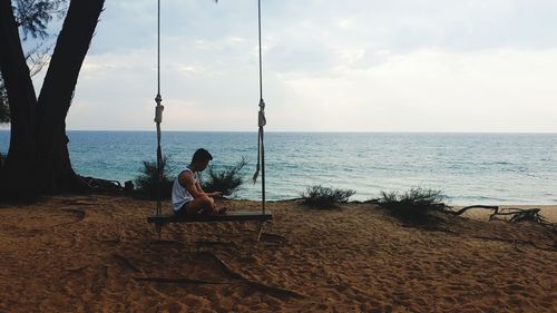 Man sitting on shore at beach against sky