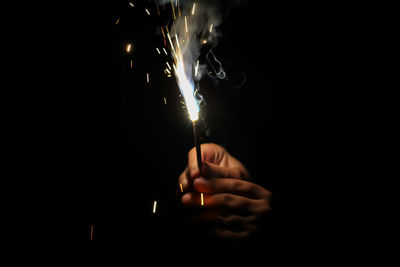 Close-up of hand holding illuminated sparkle against black background