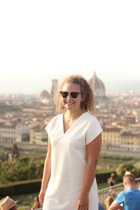 Portrait of young woman standing in city against sky