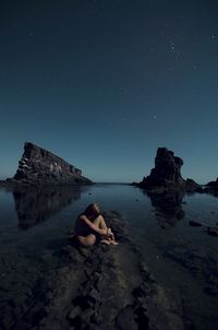 Side view of naked woman hugging self at rocky shore