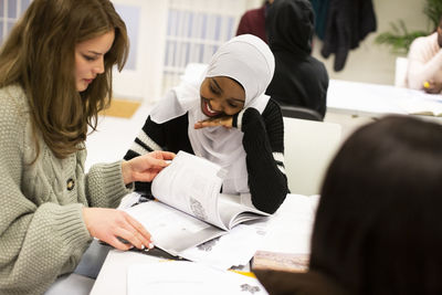 Friends discussing while sharing book in classroom