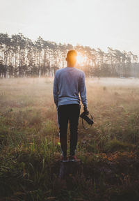 Rear view of man walking on field at sunset