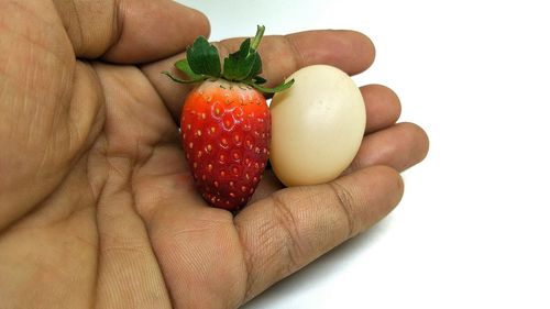 Cropped image of hand holding strawberry against white background