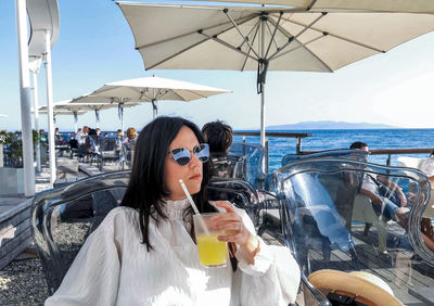 Portrait of beautiful and stylish young woman drinking cold drink in bar on sea shore.