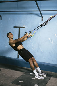 Full length of shirtless man holding umbrella against wall