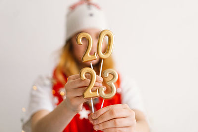 Funny young girl in a new year's hat and red scarf holds the numbers 2023 in her hands.