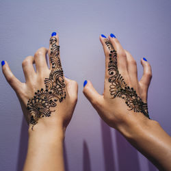 Cropped hands of woman with henna tattoo by wall