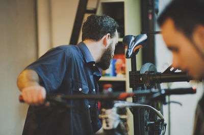 Mechanic repairing bicycle while customer standing at workshop
