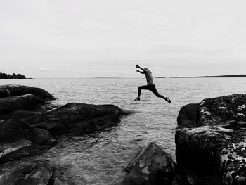 Man jumping on rock at sea shore against sky