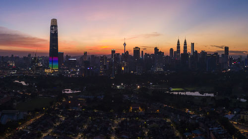 Illuminated buildings in city against sky during sunset