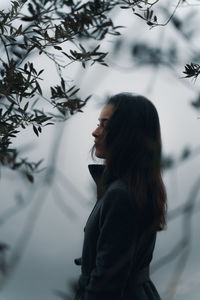 Side view of woman between trees against fog