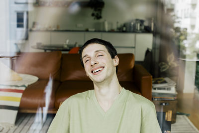 Happy young man enjoying at home seen through glass window