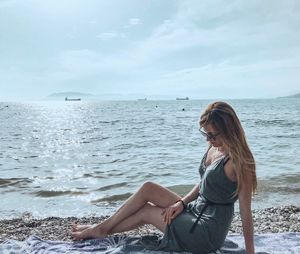 Woman sitting on shore at beach against sky