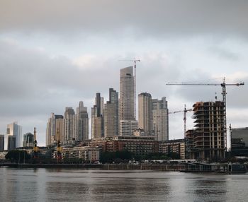 Modern buildings by river against sky in city