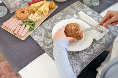 High angle view of woman hand cutting bread in plate on table 