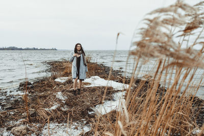 Young woman standing on shore against sky