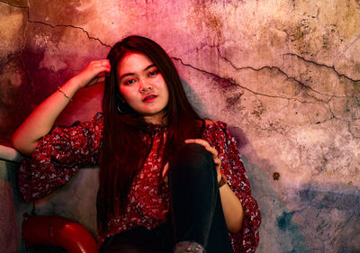 Portrait of young woman sitting against wall