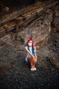 Full length of woman wearing mask sitting on rock formation