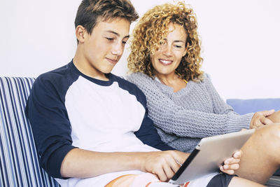 Son showing digital tablet to mother while sitting on sofa at home