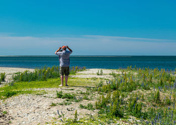 Rear view of woman standing at beach against sky