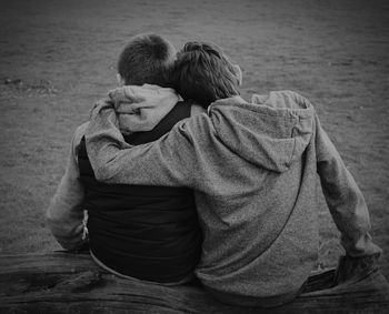 Rear view of boys sitting on wood at field