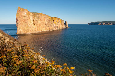 Rock formations by sea against clear blue sky