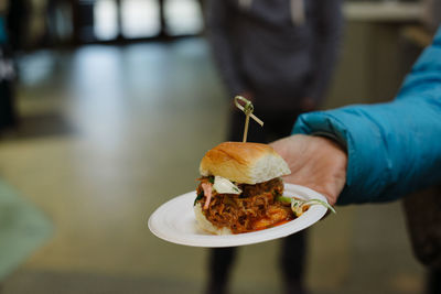 Cropped hand of woman holding burger in plate