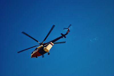 Low angle view of helicopter flying against blue sky