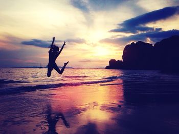 Silhouette woman enjoying on beach against sky at dusk