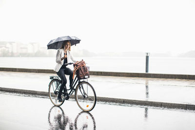 Man riding bicycle on wet road against sky during rainy season