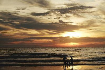 Silhouette people on beach against sky during sunset