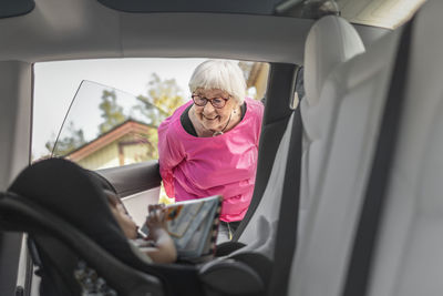 Grandmother looking at baby girl sitting inside car