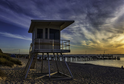 Lifeguard hut on beach against sky during sunset