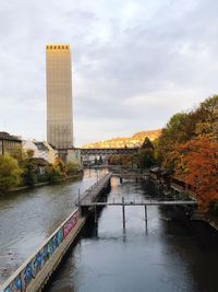 Bridge over river by buildings against sky during autumn