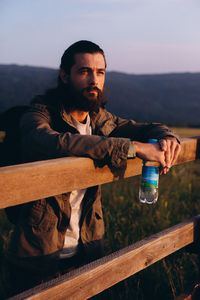 Young man sitting on railing against sky