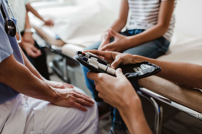 Cropped hands of nurse holding glaucometer by doctor while boy sitting in medical examination room