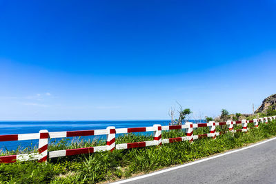 Empty road by sea against blue sky